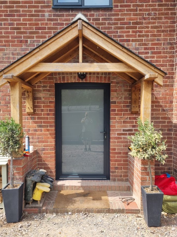 Front door with a wooden overhang, flanked by two potted plants on either side.