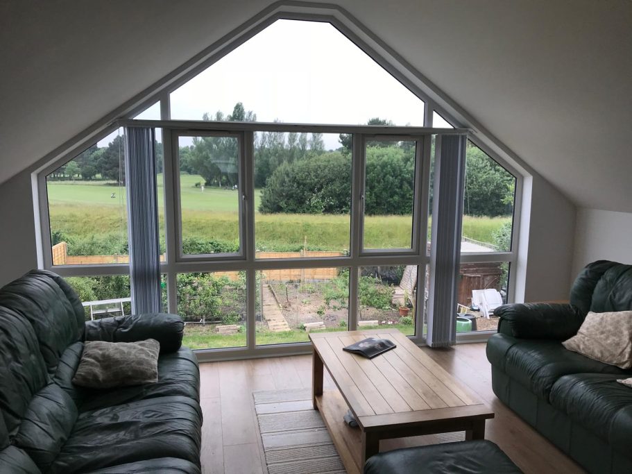 Living room with green sofas, wooden coffee table, and large windows overlooking a garden.
