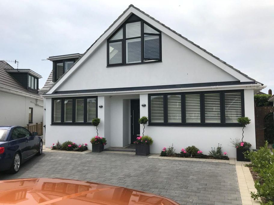Modern white house with black windows, flower pots, and a paved driveway.