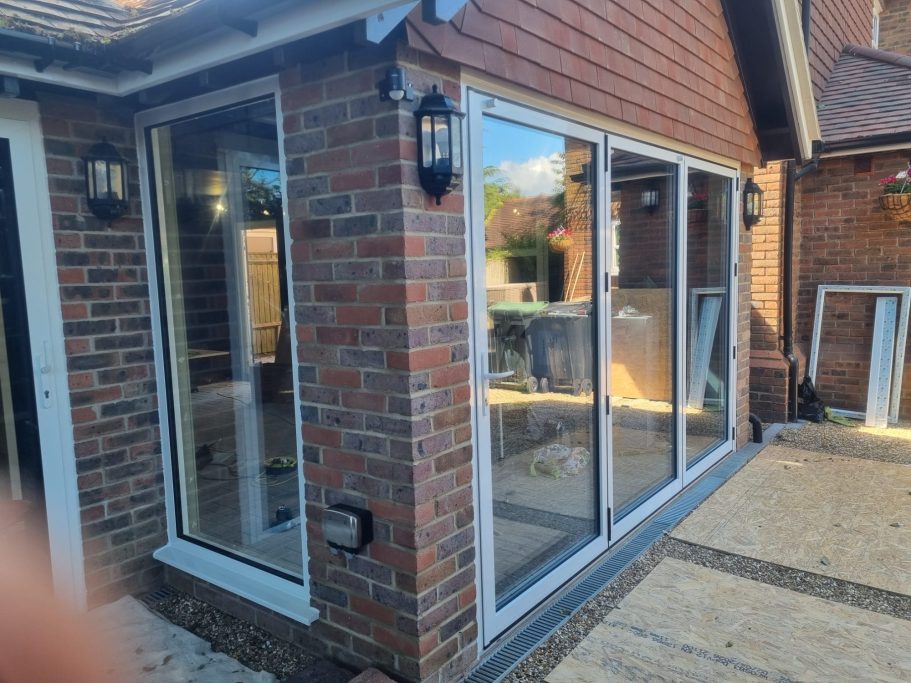 Modern brick house corner with large windows and patio area, partially in shade.