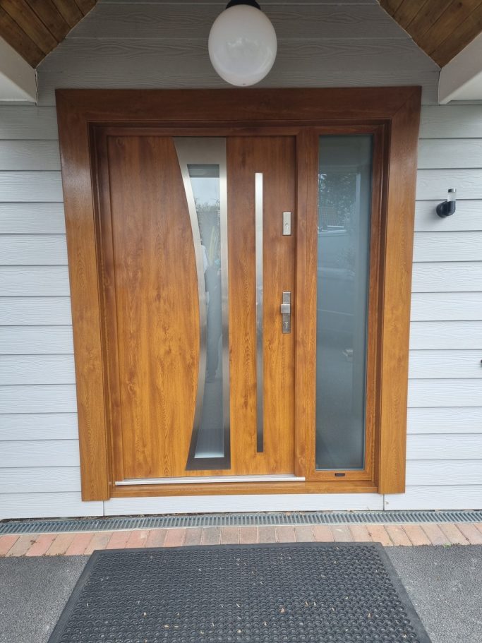 Modern wooden front door with glass panels and a sleek design, set against a light-coloured wall.