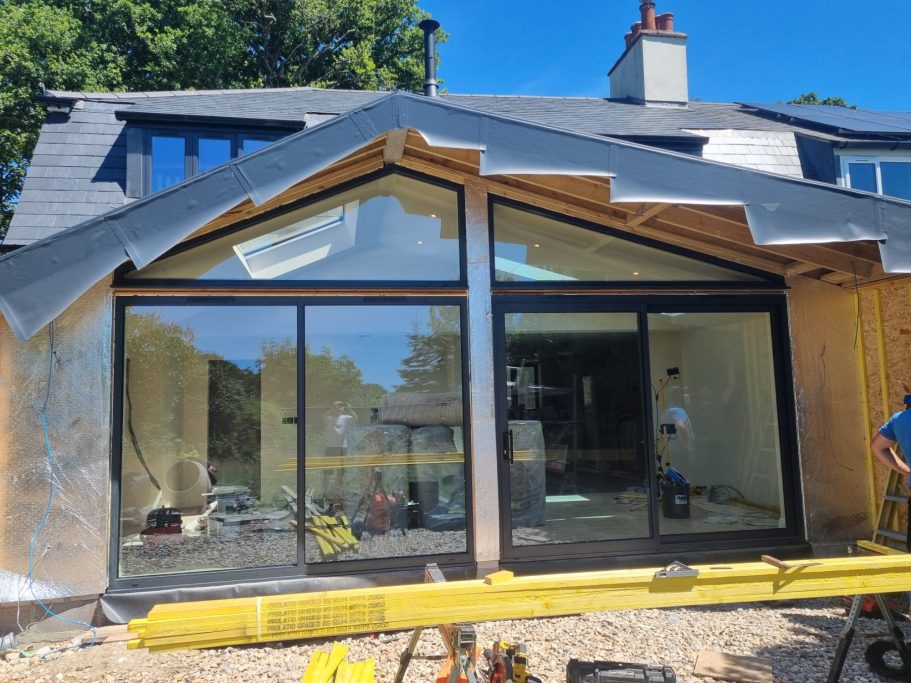 Modern wooden structure with large glass windows and a sloped roof under a clear blue sky.