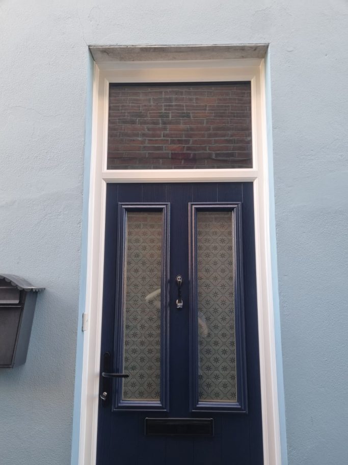 Blue door with a window above, featuring a geometric design and a letterbox to the side.