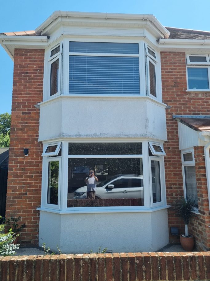 A two-storey brick house featuring large bay windows and a car visible outside.
