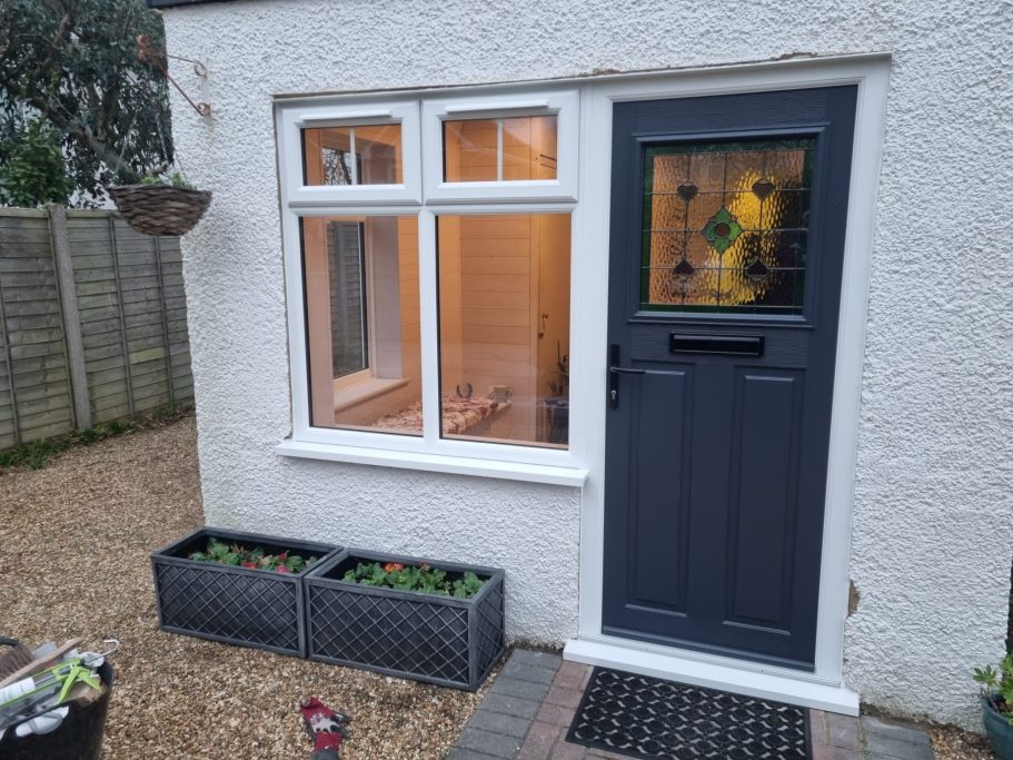 A modern front door with glass panel beside a window and planters on the ground.
