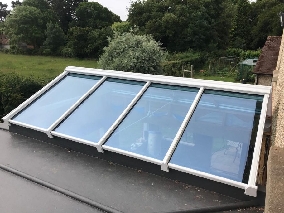 Flat roof with four large glass skylights overlooking green trees.