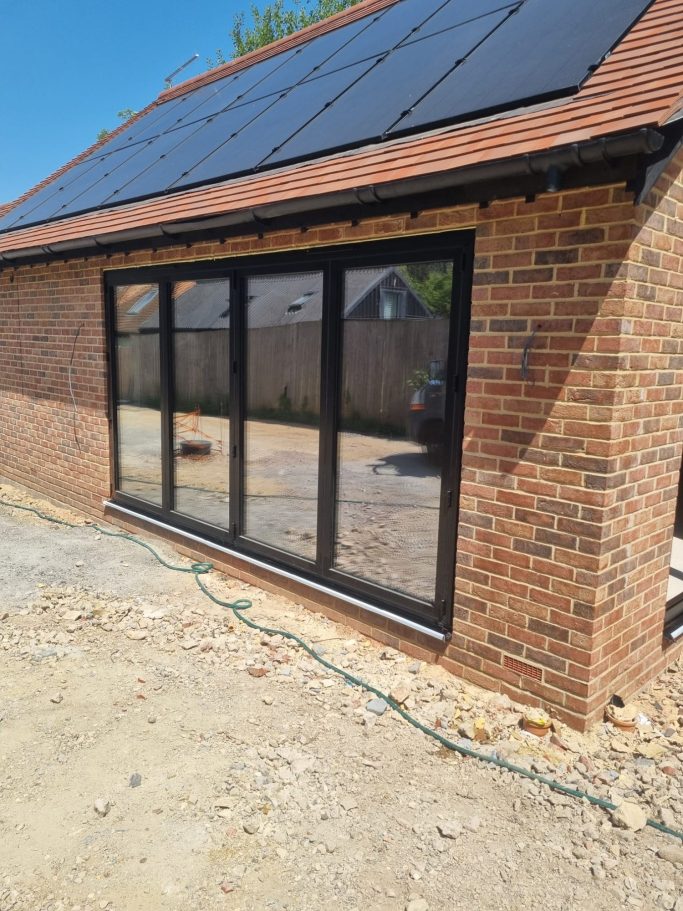 Newly built brick extension with large black-framed windows and solar panels on the roof.